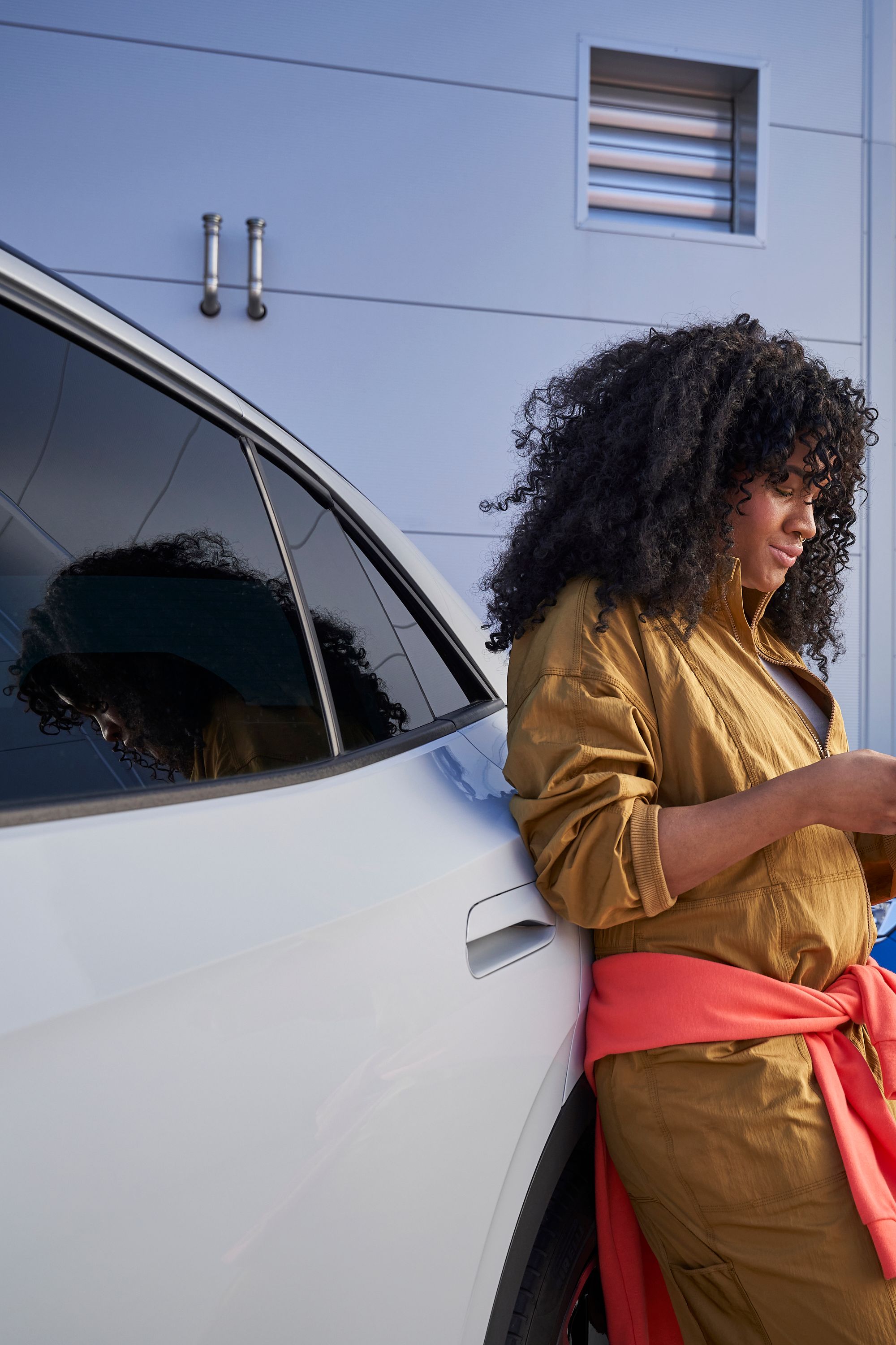 Frau lehnt an Volkswagen und blickt auf ihr Smartphone, im Hintergrund sieht man einen blauen T-Roc