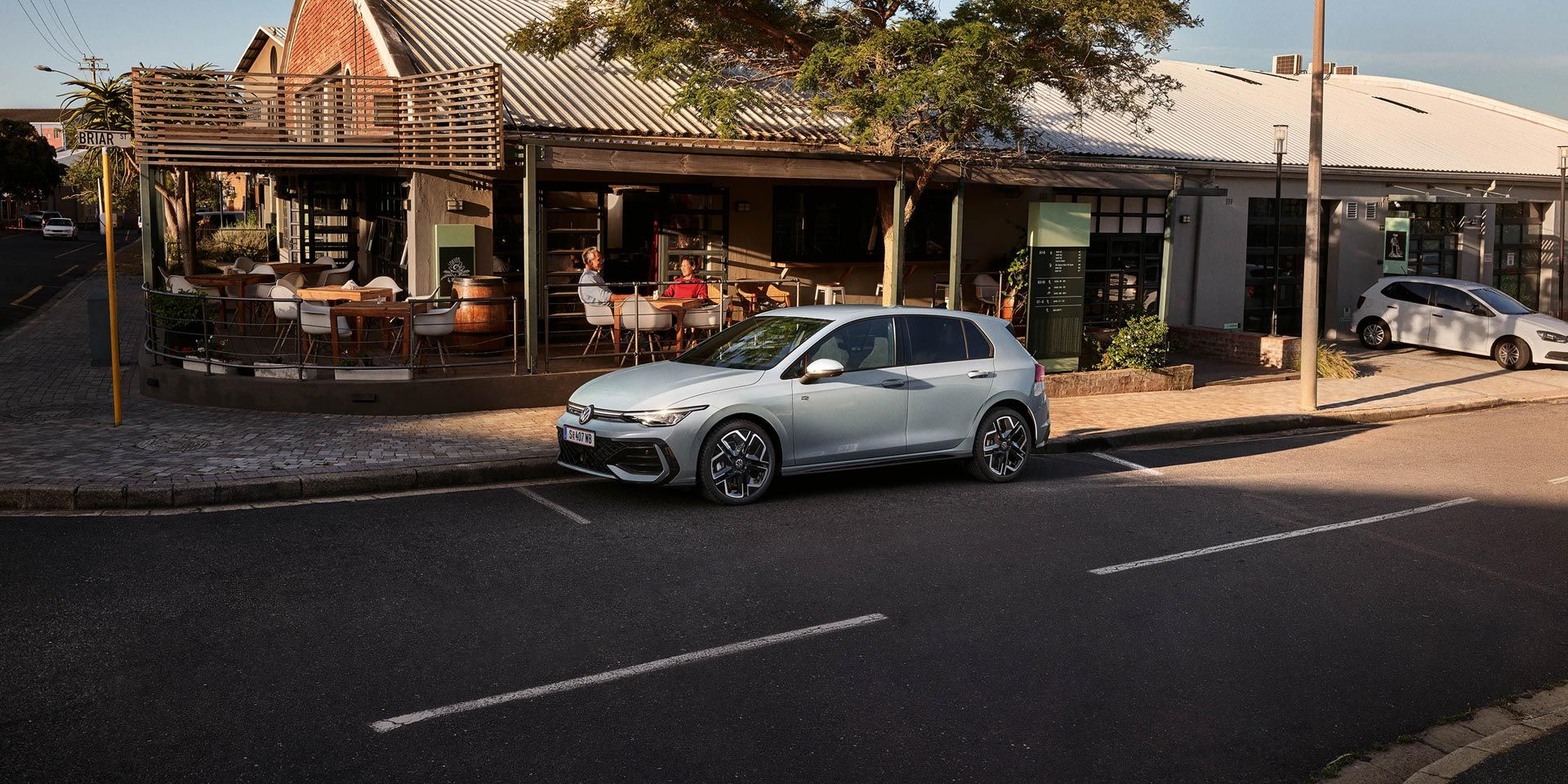 Un Golf R-Line alb parchează lateral în fața unui restaurant.