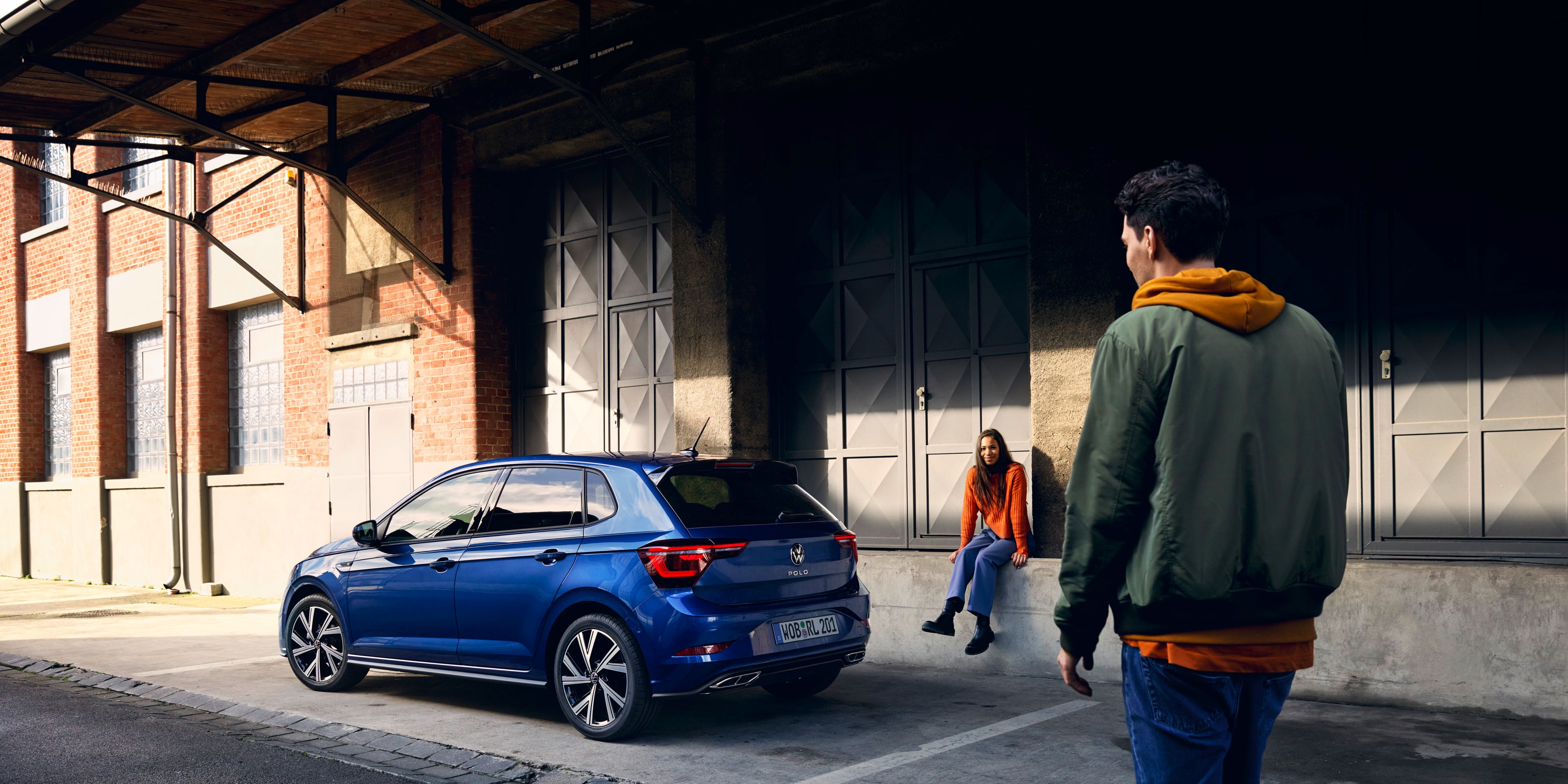 Ein blauer VW Polo steht vor einer Rampe, ein Mann geht am Heck mit den optionalen LED-Rückleuchten vorbei. 