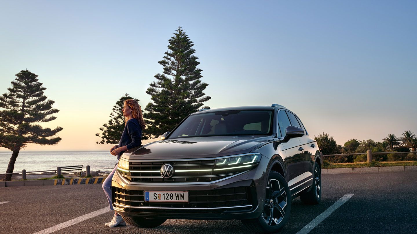 Un VW Touareg Elegance în lumina apusului, la mare, cu faruri HD Matrix aprinse. 