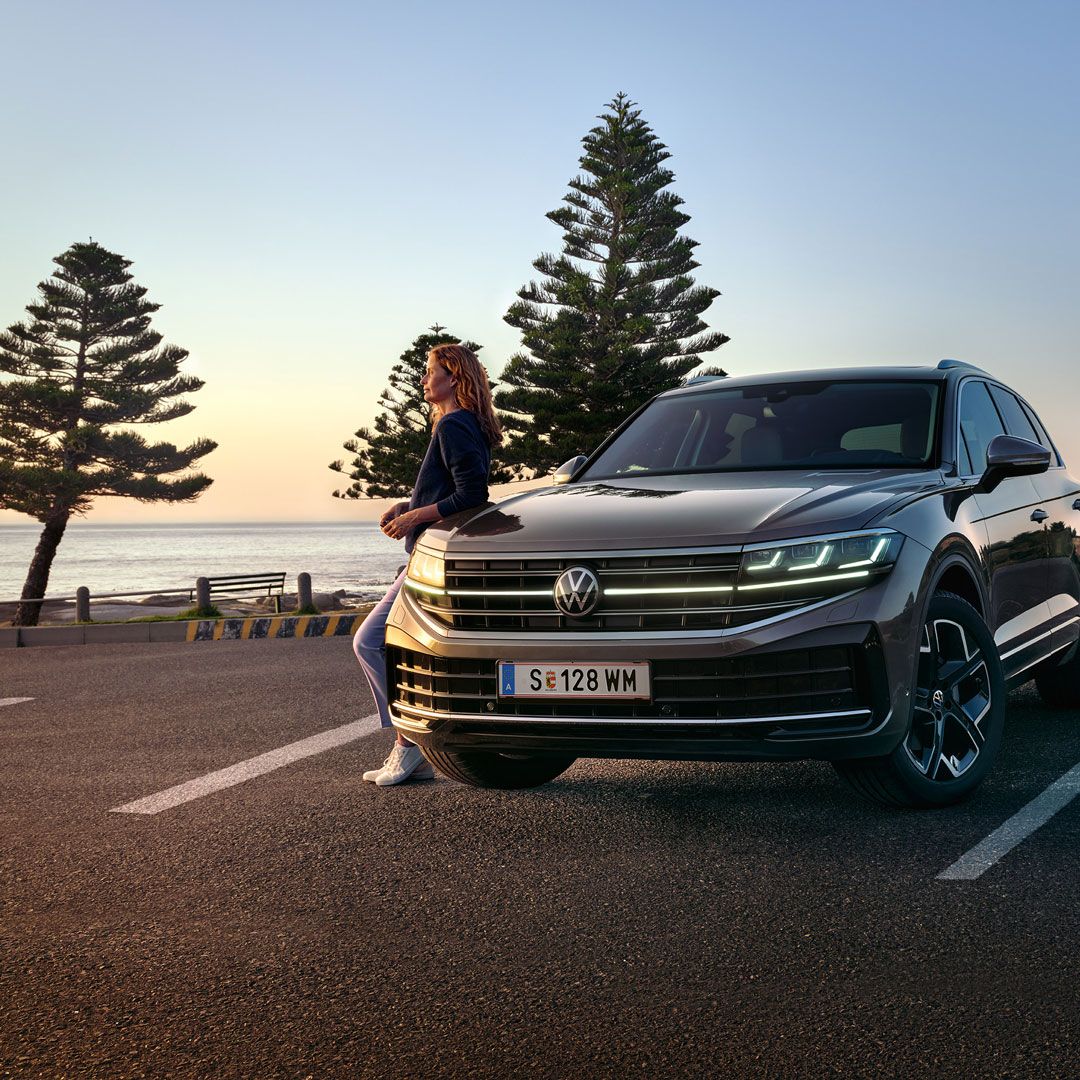 Un VW Touareg Elegance în lumina apusului, la mare, cu faruri HD Matrix aprinse. 