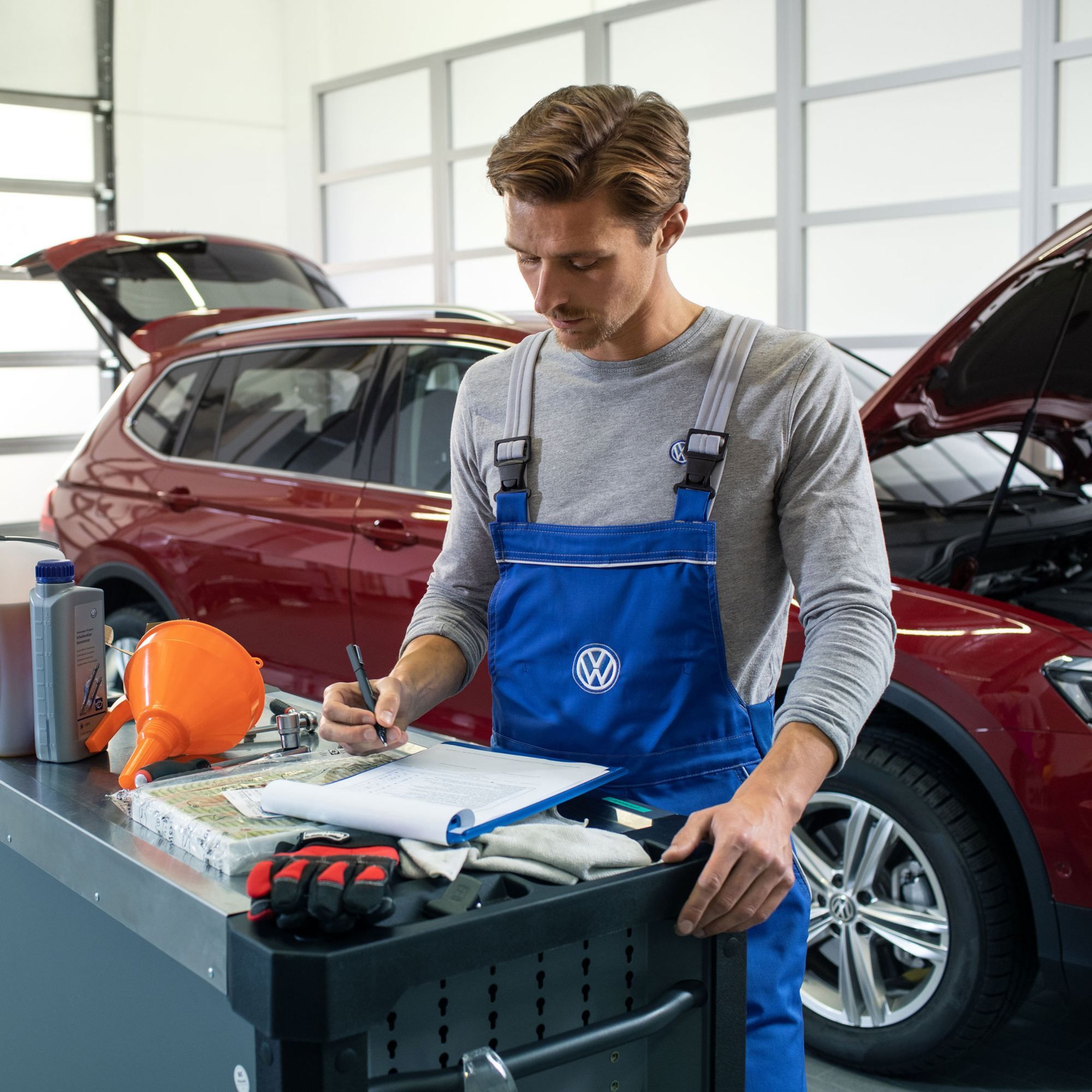 Ein VW Servicemitarbeiter vor einem roten Volkswagen mit Dieselmotor und einer geöffneten Motorhaube in einer Werkstatt