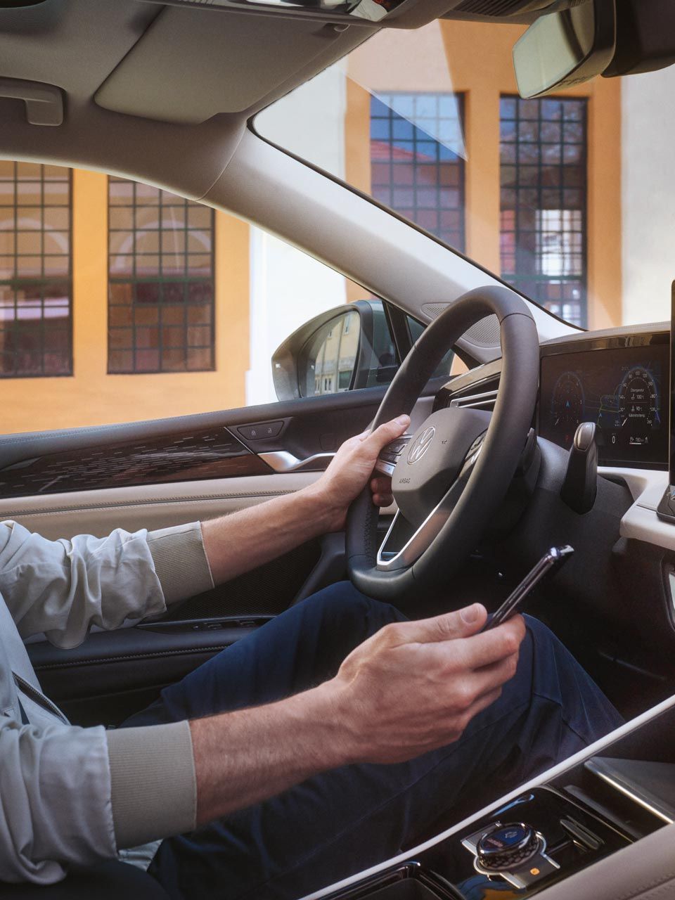 Fotografie din interiorul unui VW Tiguan. Un bărbat aflat pe scaunul șoferului controlează cu smartphone-ul său aplicația opțională VW Connect Plus.