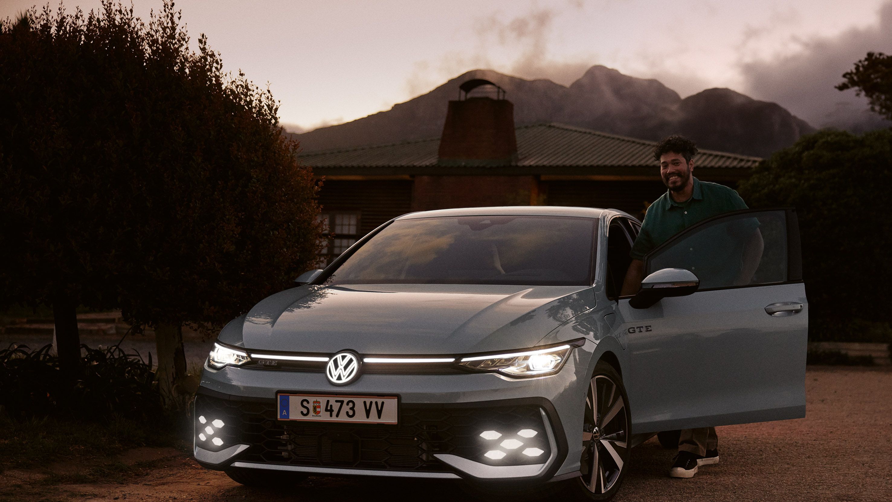 Vedere laterală VW Golf alb, parcat lângă un restaurant. Un bărbat se deplasează de la ușa restaurantului în direcția mașinii.