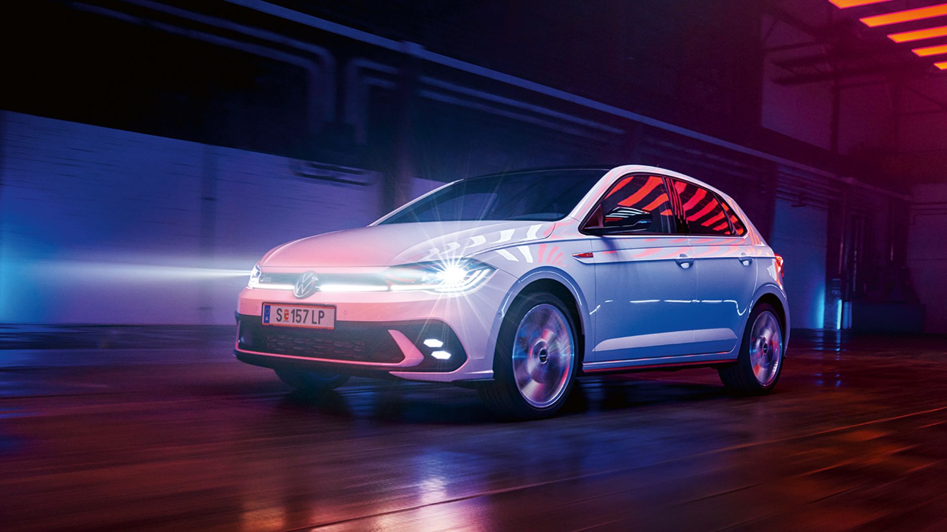 Ein weißer VW Polo GTI fährt in einer Halle mit eingeschalteten LED-Matrix-Scheinwerfern und Lichtleiste in der Front