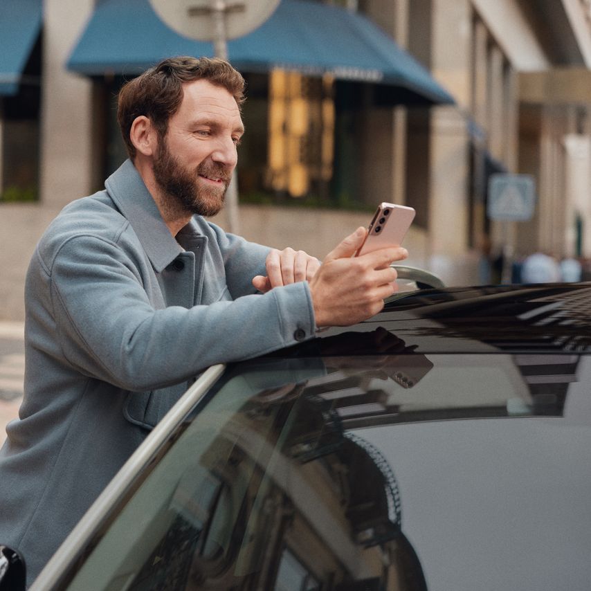 Mann lehnt an einem Volkswagen und schaut auf sein Mobiltelefon