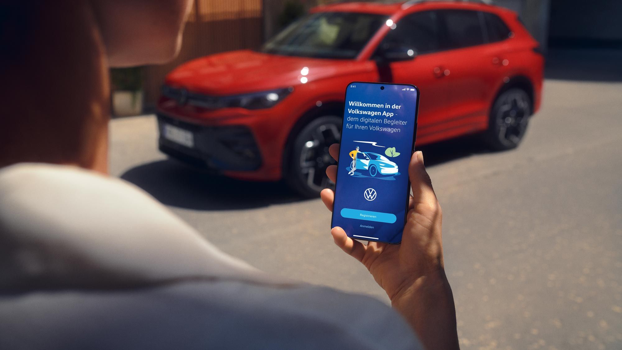 Vedere a unui afișaj de telefon mobil cu datele modelului Tiguan, în fundal un VW Tiguan roșu parcat lateral