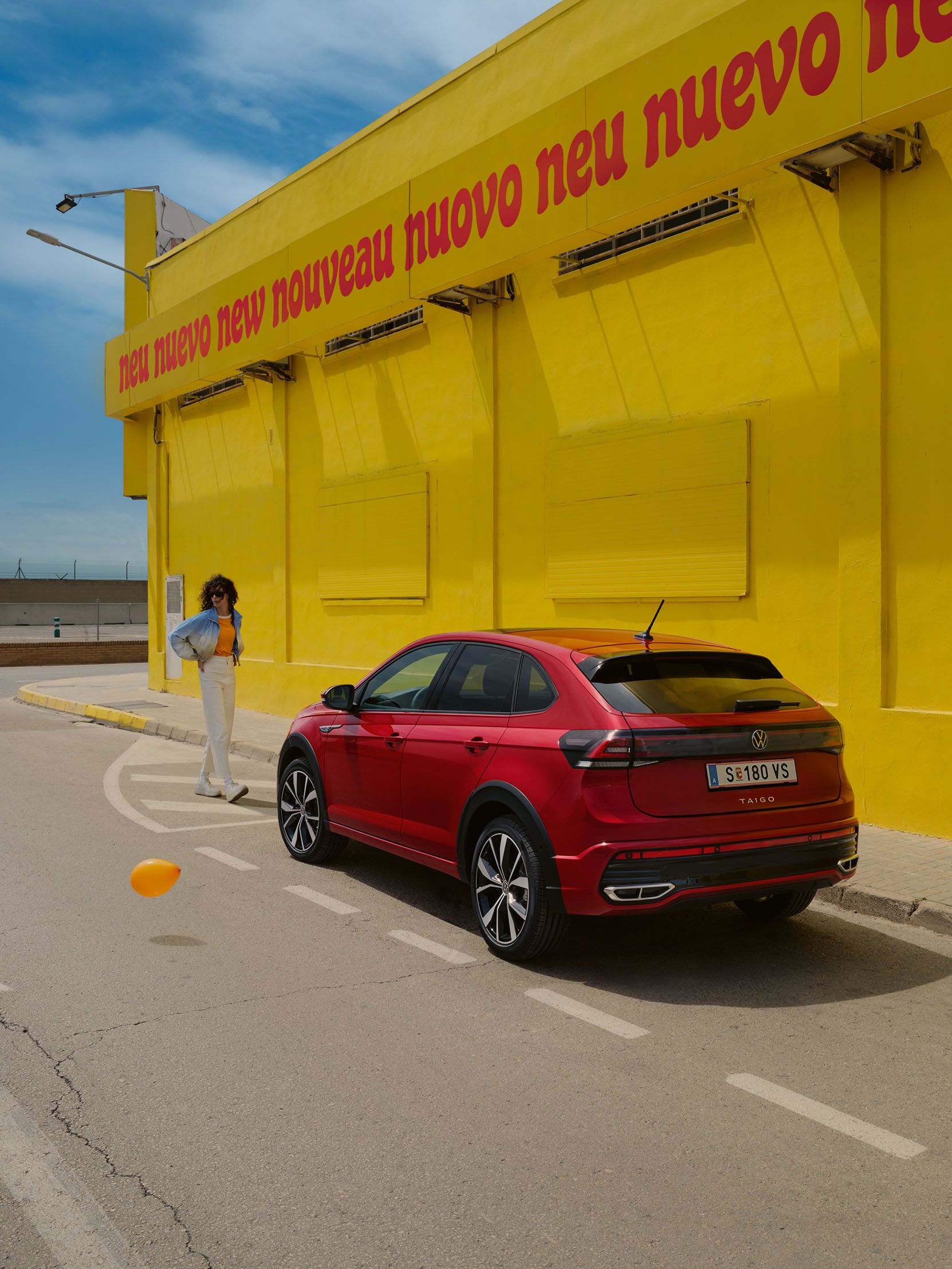 VW Taigo steht neben einem gelben Gebäude, eine Frau geht darauf zu